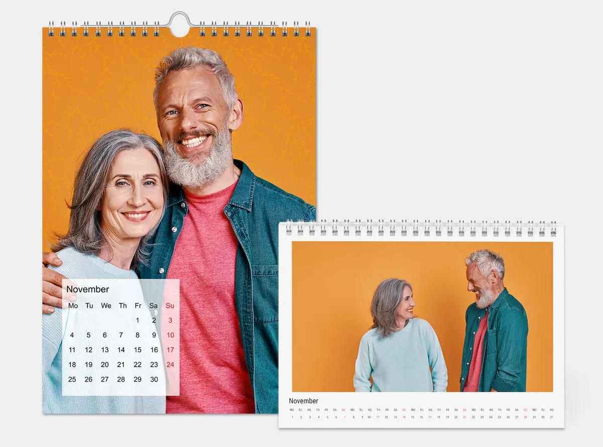 Wandkalender A4 hoch und Tischkalender auf einem grauen Hintergrund. Die Kalender sind mit Paarfotos gestaltet und zeigen viel Orange.